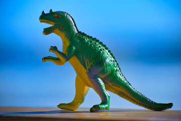 Dinosaur toy standing outside with the beach and ocean in the background.