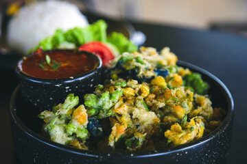 Crispy Vegetable Fritters in a black plate with Thai chili sauce on a black table with rice background, Thai food concept.
