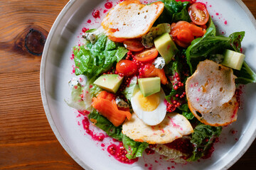 Vegetable salad with egg, tomato, pomegranate and avocado. A healthy dish on a white plate in a restaurant close-up.