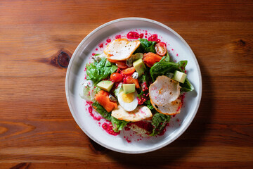 Vegetable salad with egg, tomato, pomegranate and avocado. A healthy dish on a white plate in a restaurant.