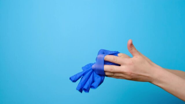 Close up of unrecognizable young woman removes medical gloves and throw it in trash, isolated on blue studio background with copy space for advertisement. Concept end of virus epidemic 