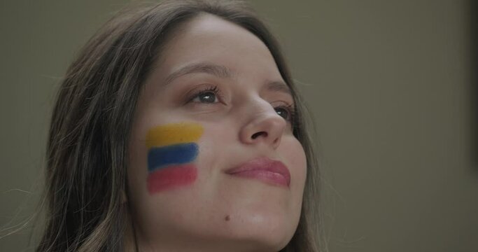 Close up portrait of young pretty blonde girl with Colombian flag face paint on her cheek relaxed and smiling