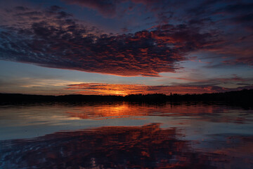 Fototapeta na wymiar Reflection of textured sunset clouds on lake