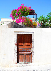A typical door in a white wall with bougainvillea flower above in the traditional village of Megalochori in Santorini, Greece.