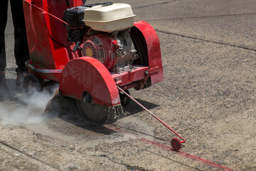 Concrete Road Cutters with worker. Worker using diamond saw blade machine cutting concrete road at...