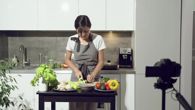 Attractive young woman recording a video about healthy eating on digital camera in the kitchen at home. Vlogging and social media concept