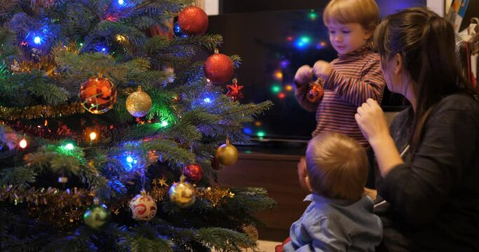 Mother and children, baby and bother decorate Christmas tree