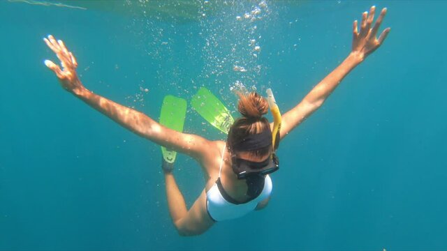 Slow motion shot of young woman snorkeling over coral reef in blue sea - Wakatobi Regency, Indonesia