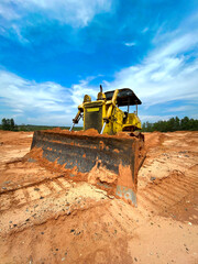 Yellow bulldozer on the sand, with a bright beautiful blue sky on the background