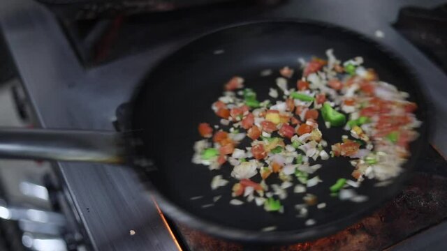 Cooking red sauce, with sauteed vegetables, caramelised onions, red chillies and capsicum on a hot oil pan.