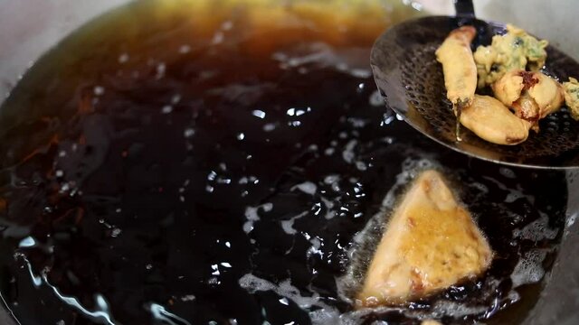 Making indian style fritters or bread pakoda by deep frying vegetables stuffed marinated bread in hot oil kadhai.