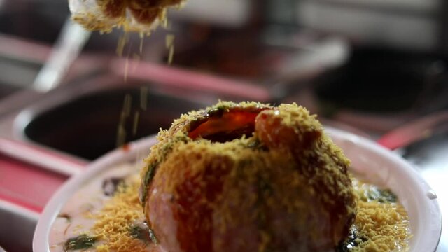 Making indian style street chaat and raj kachori with topped spices, red sauce and corns. 