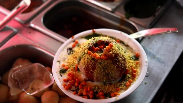 Making indian style street chaat and raj kachori with topped spices, red sauce and corns. 