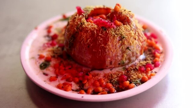 Making indian style street chaat and raj kachori with topped spices, red sauce and corns. 