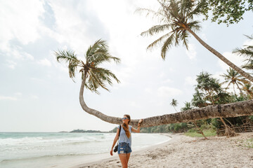 Happy tourist  woman photographer stand on the beach near palm tree with hand holding camera. Summer vacation