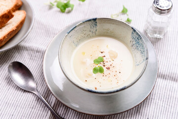 Cauliflower and Potato Cream Soup served with herbs and pepper on white linen striped tablecloth. Selective focus