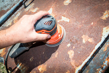 Man's hand operates a disc/orbital sander, to remove paint and rust from metal doors