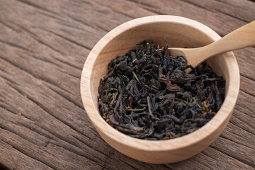 Chinese leaf tea in a wood bowl on grained wood background
