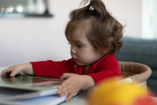 Bebe sentada na cadeira próxima a mesa e brincando com um caderno universitário