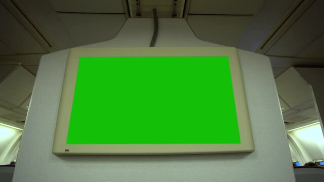 View from passenger seat in airplane at blank empty big green screen monitor attached to wall of plane.