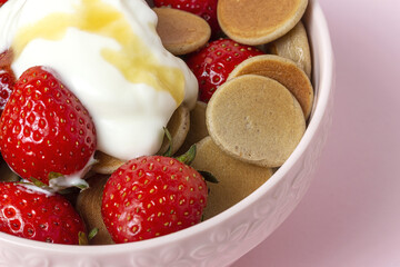 Homemade cereals mini pancake with yogurt, honey and strawberries on colorful background.