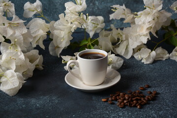 Composition with white cup of coffee , beans  and flowers as background