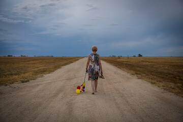 Woman walking on dirt road after party holding balloons and shoes