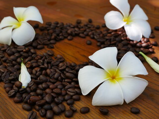Fototapeta na wymiar Coffee beans on a wooden floor adorned with white plumeria flowers.