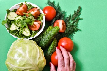 Healthy eating female hand holds a tomato. cabbage, tomato, cucumbers on a green background. diet concept.