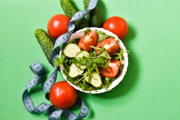 Healthy nutrition. Salad with arugula, tomatoes and cucumbers with measuring tape on a green background. concept of diet, healthy eating.