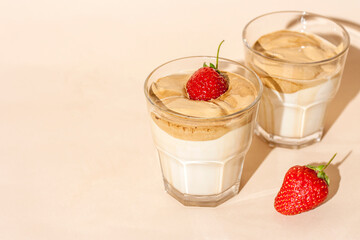 Dalgon coffee in a transparent glass with milk on a pastel background with strawberries. Copy space