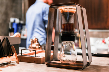 Male barista making pour-over coffee with alternative method called Dripping. Close up modern Coffee grinder, coffee stand and pour-over on concrete top counter.