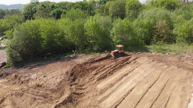 Aerial view of bulldozer flattening surface on further construction site