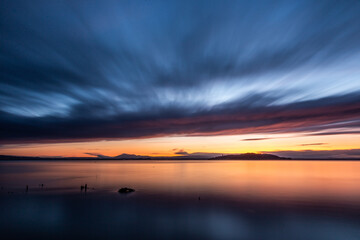 Sunset a Trasimeno lake (Umbria, Italy), with fishing net poles and branches on perfectly still water