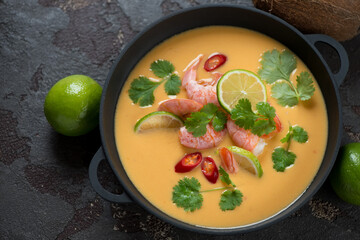 Thai-style pumpkin, coconut milk and prawn soup in a cast-iron pan, horizontal shot on a brown stone background, elevated view