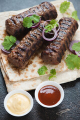 Close-up of bbq marbled beef kabobs with lavash flatbread, fresh cilantro, red onion and dips, vertical shot, selective focus