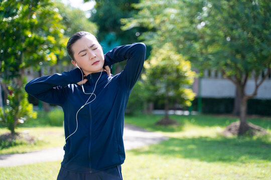 Portrait of Asian woman wearing earphones listening to music was sick with body pain at park.