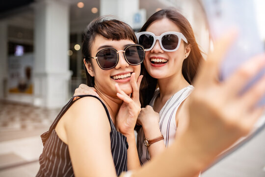 Attractive beautiful asian friends women using smartphone. Happy woman with shopping .urban city while taking self portraits with friends together. Girl  holding colour  bag.Friends walking in mall.
