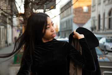 portrait of 20s long hair cool young African woman holding black coat standing nearby the street building in the city