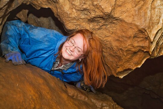 Red-haired girl-caver smiles in the cave.