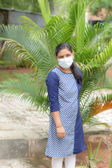 an indian lady is standing in garden with wearing face mask due to covid 19 pandemic