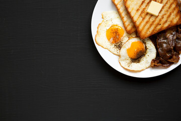 Homemade Healthy Sunnyside Eggs Breakfast on a white plate on a black background, top view. Flat lay, overhead, from above. Copy space.