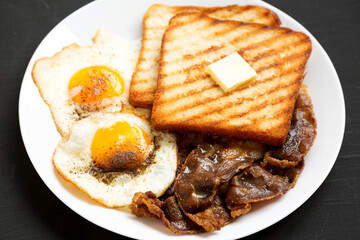 Homemade Healthy Sunnyside Eggs Breakfast on a white plate on a black background, low angle view. Close-up.