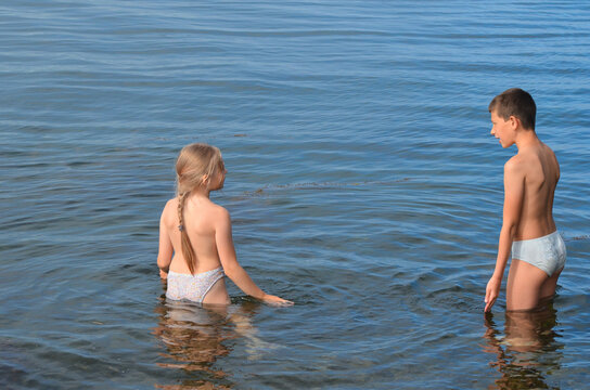 Two children are standing in waist-deep cool water. Opening of the swimming season