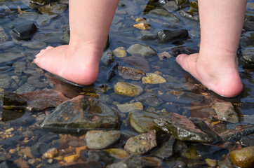 Child's feet close-up walking on water on rocks. Exercises for health and tempering. Prevention of...