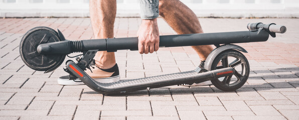 Unrecognizable man holding folding electric scooter in summer outdoor.