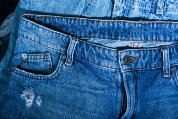 Blue jeans pants clothes pile background. Stack of blue jeans on shop desk,Denim jeans background. Destroyed torn classic denim blue jeans patches, banner fashion background