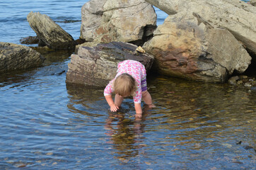 A child is barefoot on the water in summer on a rocky beach. Active leisure lifestyle