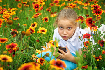 Girl with a mobile phone in nature .A happy child is relaxing outdoors in nature . Children use modern technologies for recreation, entertainment and education