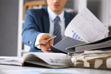 Male hands hold documents with financial statistics at office workspace closeup. White collar check...
